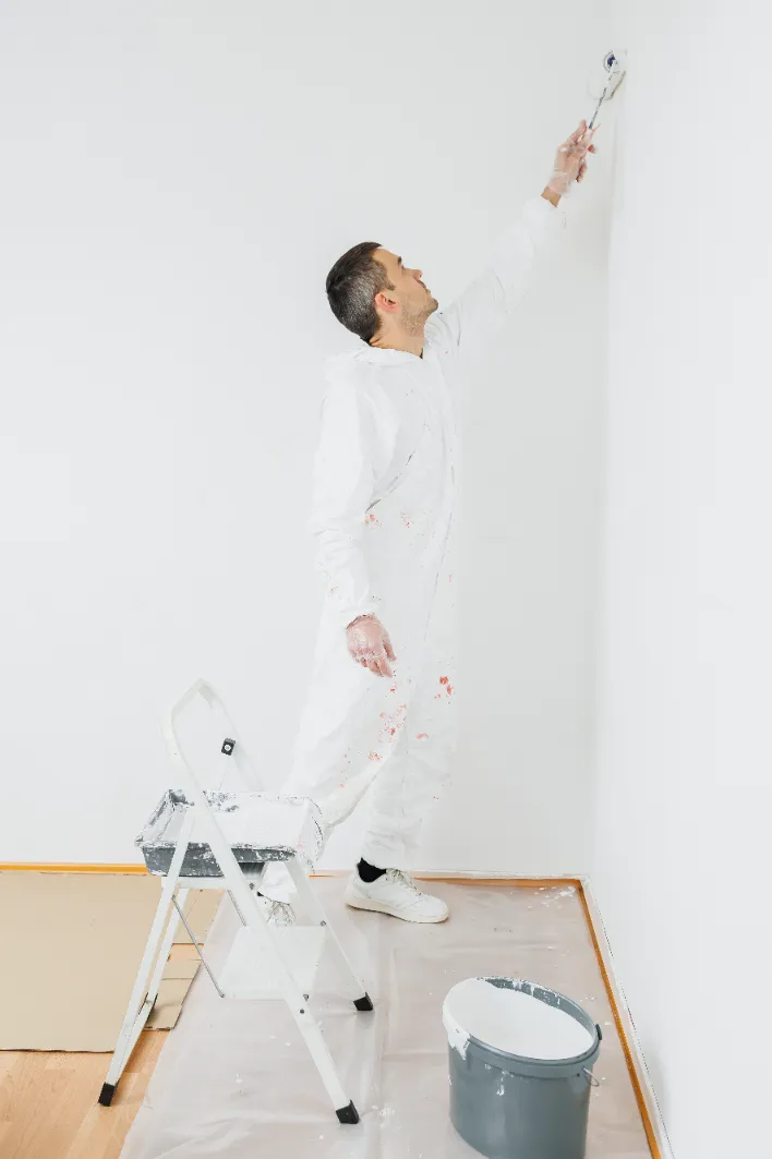 Professional painter in white coveralls painting a wall with a roller.