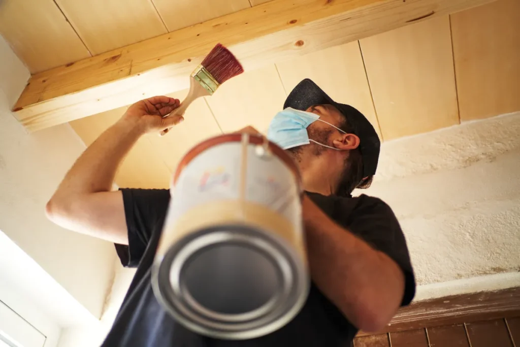 A man painting the a wooden beam of the house.