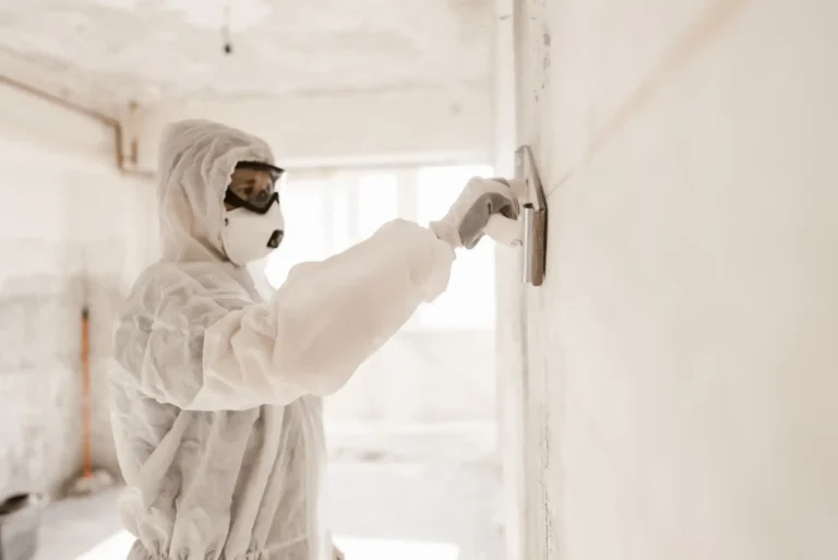 A worker covered in jumpsuit and mask carefully repairing the walls of the house.