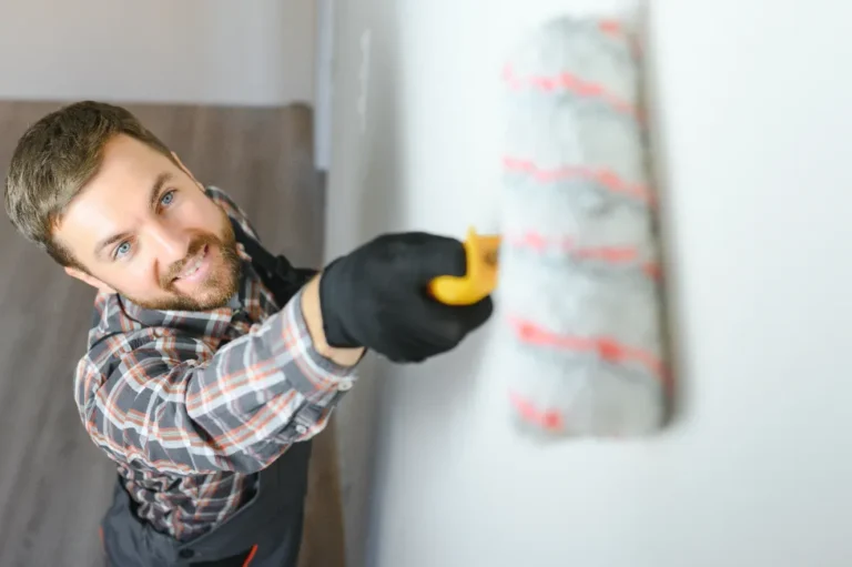 A man smiling and painting the wall with a paint-roller.