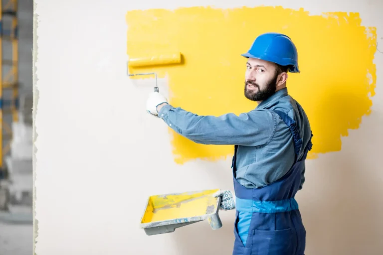 A worker looking back while painting the walls with yellow color.