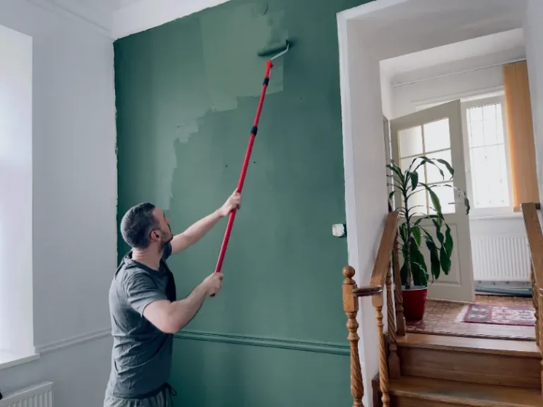 Interior painting project with a man using a roller to apply dark green paint on a living room wall.